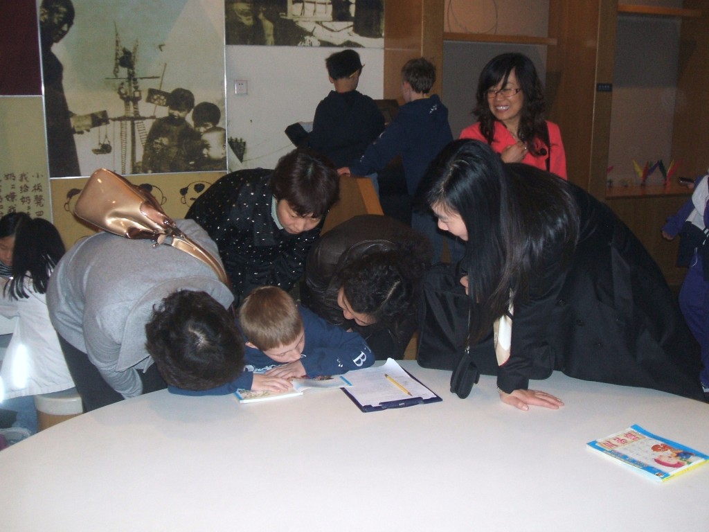 The author's son surrounded by a group of Chinese women crowded very closely around him as he bends over a book.