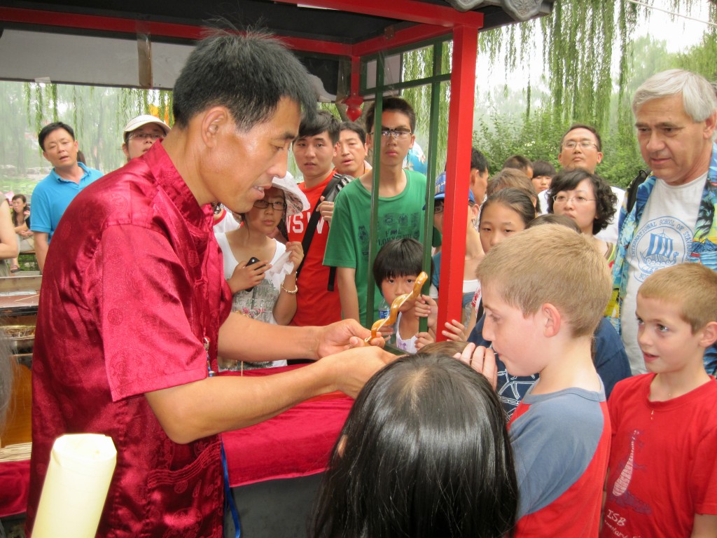 The author's son being taught to make a blown-candy animal at a cart in the Summer Palace in Beijing, surrounded by a friendly crown of Chinese onlookers.