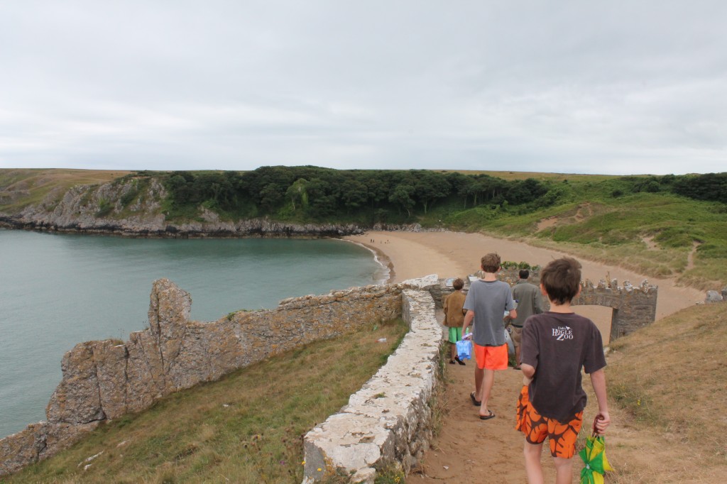 Kids walk on a narrow pathway along a cliff down to a secluded beach
