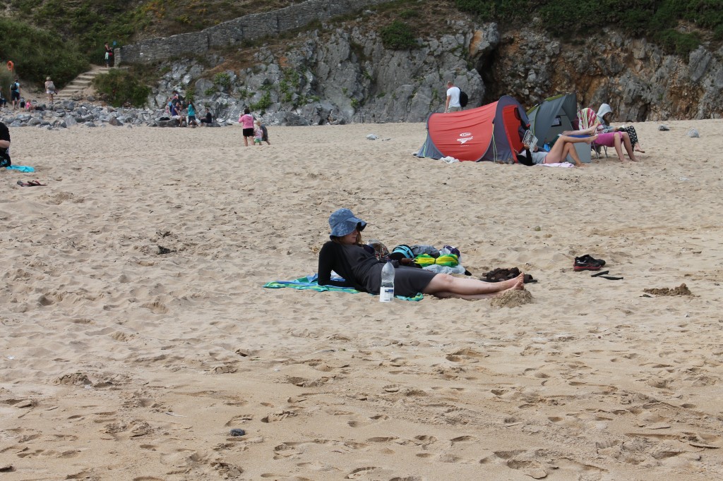 The author on a beach wearing a dress and long sweater, with several tents seen behind her on the beach.