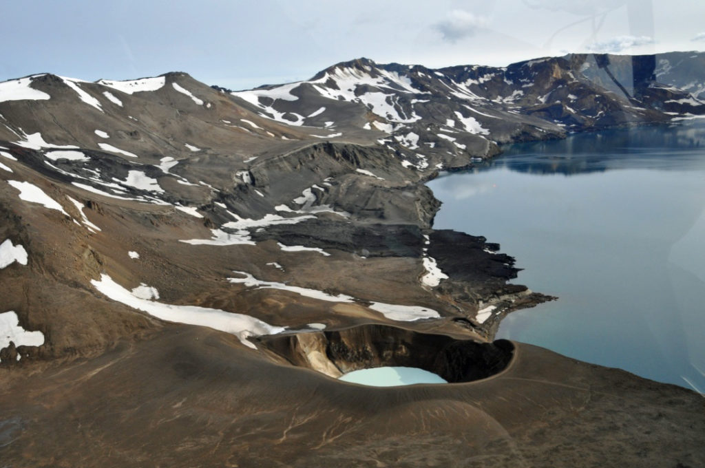 A strikingly beautiful volcanic coastline with a mirror-like lake and snow in the craters of the hills