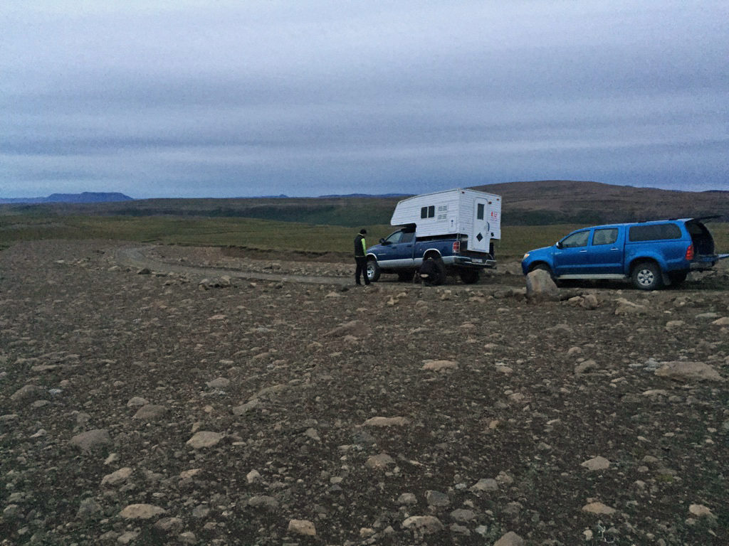 A camping trailer and a pickup truck on the side of a rocky dirt road, with no signs of habitation visible.