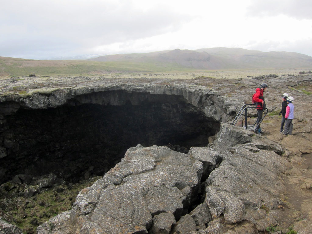The author's children stand on top of a huge cavernous hole in the ground, the interior of the cave is visible