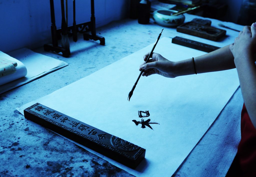 The author's daughter's hand writing Chinese characters with a calligraphy brush.
