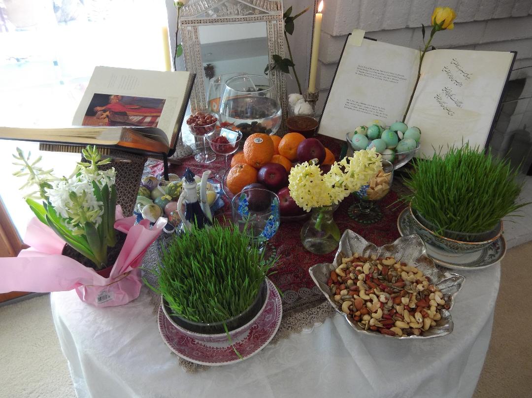 A round table covered with dishes of wheat grass, nuts, fruit, flowers, colored eggs, boks, photos, goldfish in a bowl and other traditional items.