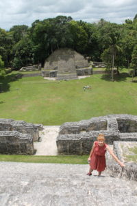 The author stands on top of a Mayan temple, with the camera looking past her over an open courtyard to another temple on the other side.